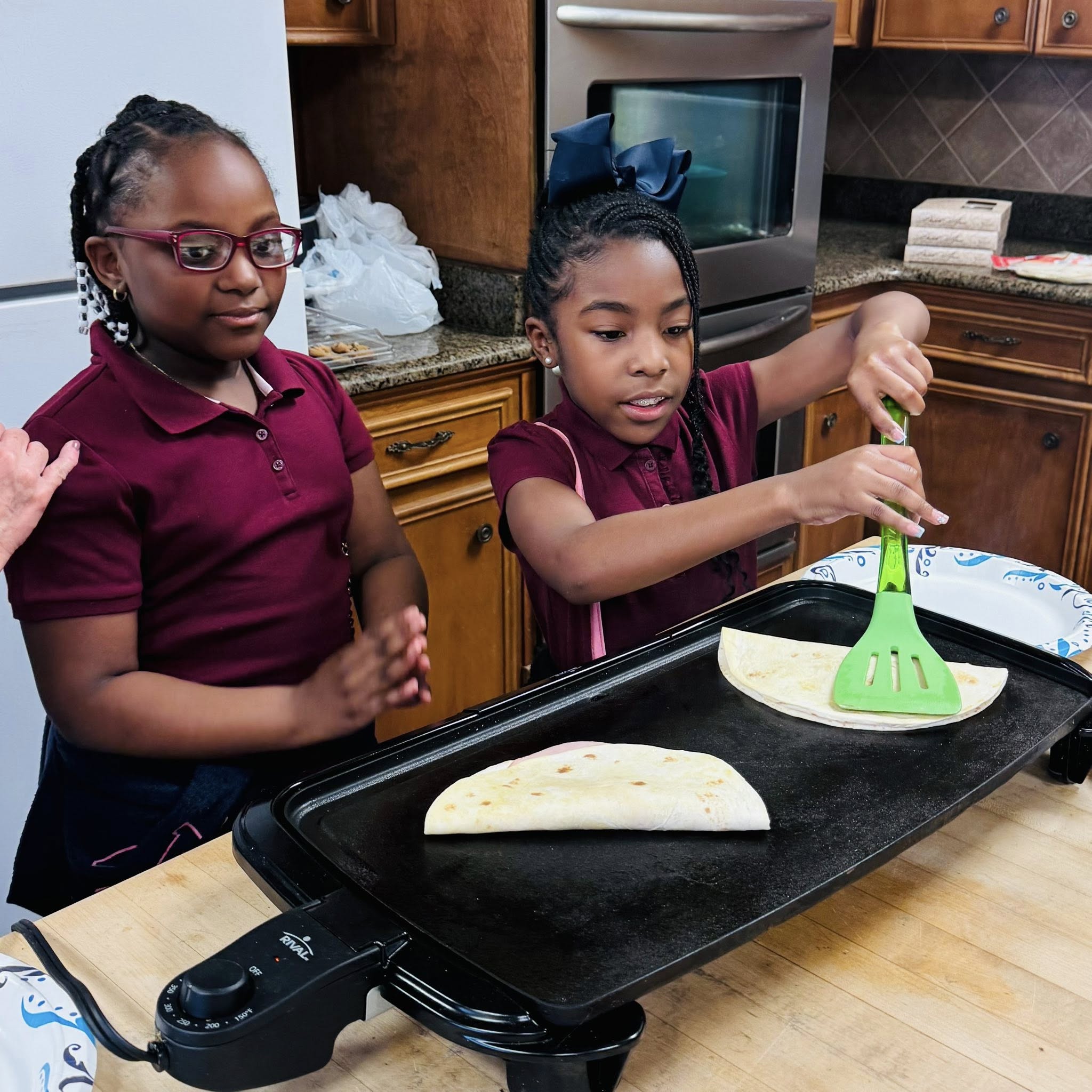 Two girls cooking quesadillas on a griddle.